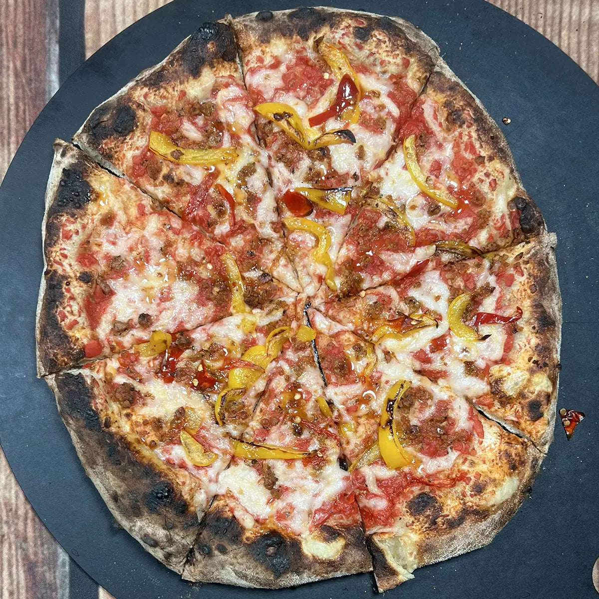 Vegan Calabrese Sausage Pizza from Fire & Char - Richmond, VA. Plant-based pizza with Be-Hive vegan mozzarella, vegan sausage crumbles, Calabrian chilis, sweet yellow peppers, and house-made Calabrian chili oil. Bold, smoky, and spicy vegan pizza in Richmond and Henrico, VA.